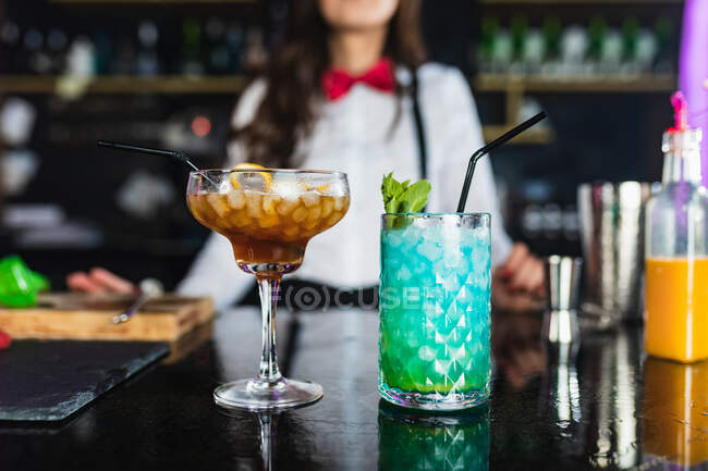 Barista donna sfocata e irriconoscibile in abiti eleganti che serve cocktail con cubetti di ghiaccio mentre si trova al bancone in un bar moderno — Foto stock