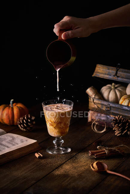 Ernte anonyme Person, die Milch aus kleinen Kannen zum Glas mit Kürbis-Gewürz-Latte am herbstlichen Dekorationstisch hinzufügt — Stockfoto