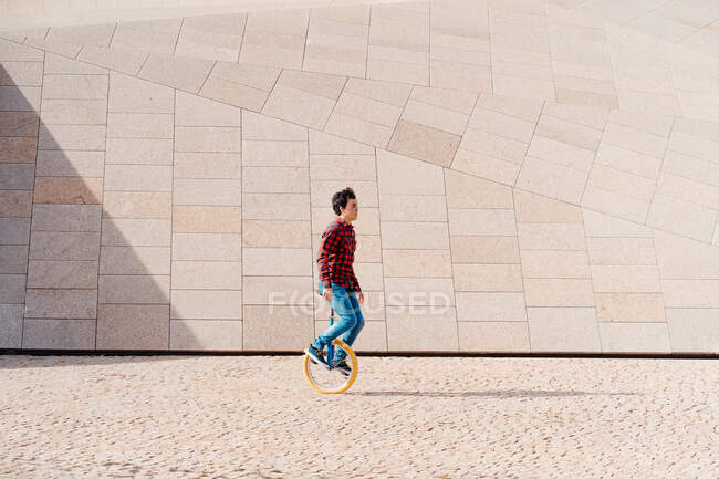 Vista laterale del monociclo maschile contro la costruzione contemporanea in pietra di insolita forma geometrica — Foto stock