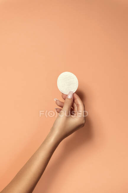 Crop unrecognizable woman with manicure and delicate skin demonstrating clean cotton pad on beige background — Stock Photo