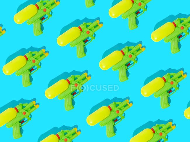 Blick von oben auf den Hintergrund, der helle Plastikspielzeugpistolen auf blauer Oberfläche mit Schattierungen darstellt — Stockfoto