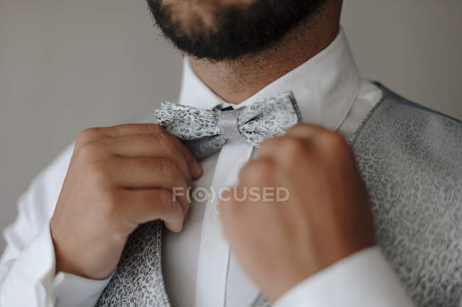 Cortar homem barbudo irreconhecível em elegante colete elegante e camisa branca ajustando gravata arco enquanto se prepara para a celebração do casamento — Fotografia de Stock