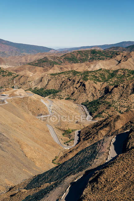 З верху порожньої асфальтової звивистої дороги на потужних брунатних пагорбах у сонячний день у Марокко. — стокове фото