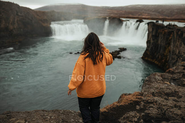 Mujer vista trasera entre tierras salvajes con cascada - foto de stock