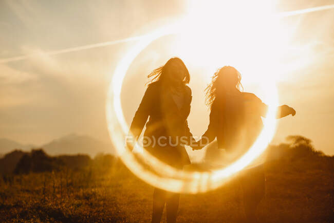 Namoradas segurando as mãos suavemente em pé no brilho da lente de luz do pôr do sol na natureza — Fotografia de Stock