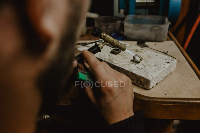 Анонимный мужчина-ювелир, использующий файл для формирования металлического кольца на верстаке в мастерской — стоковое фото