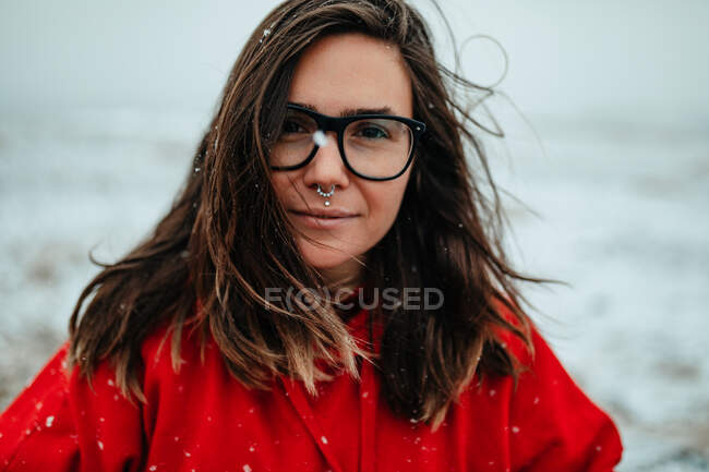 Giovane turista felice in occhiali con piercing guardando la fotocamera tra terreno deserto nella neve — Foto stock
