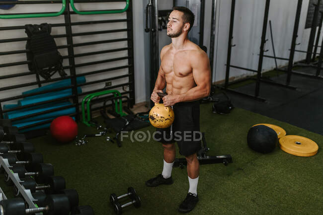 Athletic male with naked torso doing exercises with heavy kettlebell during active training in sports center — Stock Photo