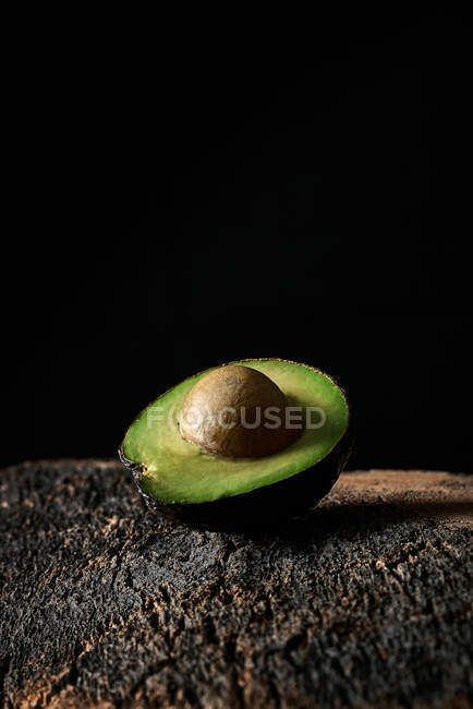 Половина стиглого авокадо з насінням, розміщеним на грубій поверхні на чорному тлі — стокове фото