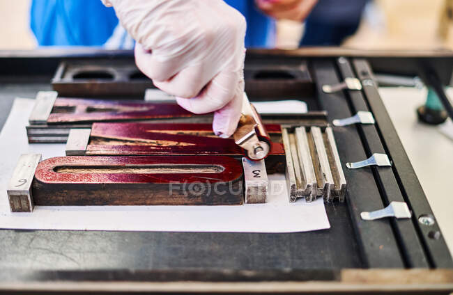 Cultivo irreconocible trabajador masculino pintura tipografía fuente con rodillo mientras trabaja en taller de impresión - foto de stock