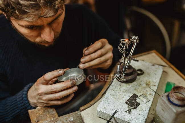 Ювелир держит незаконченное кольцо в грязных руках и проверяет качество в мастерской — стоковое фото