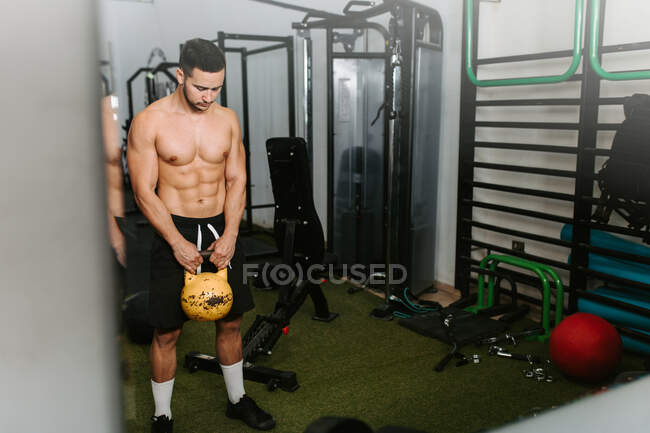 Athletischer Rüde mit nacktem Oberkörper bei Übungen mit schwerer Kettlebell während des aktiven Trainings im Sportzentrum — Stockfoto
