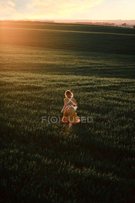 Молодая женщина в винтажном деревенском стиле платье работает в одиночку на обширном зеленом травянистом поле в летний вечер в сельской местности — стоковое фото