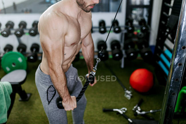 Vista lateral de los pesos pesados de elevación masculina fuerte en la máquina de ejercicio mientras entrena tríceps con cuerda - foto de stock