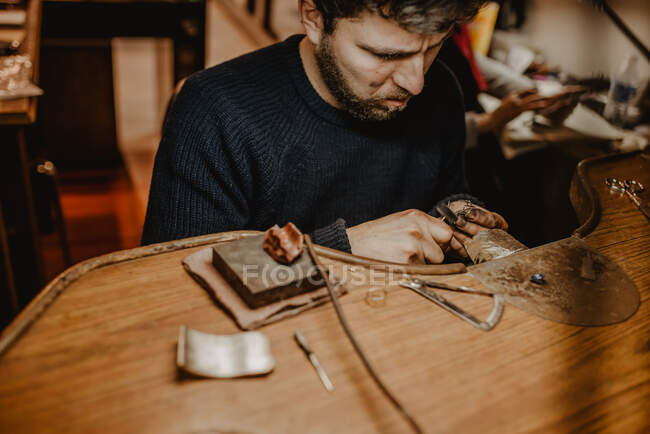 Gioielliere che utilizza la lucidatrice professionale sul banco da lavoro mentre fa anello metallico in officina — Foto stock