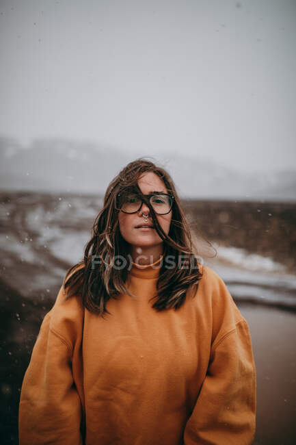 Молодий щасливий турист в окулярах з пірсингом дивиться на камеру між покинутою землею в снігу — стокове фото