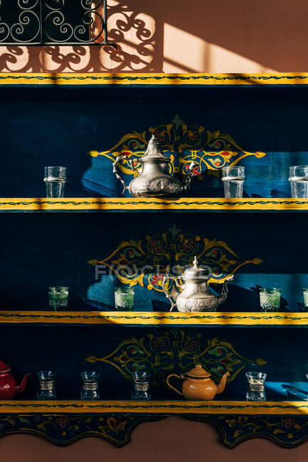 Calderas de cerámica y metal con vasos pequeños en estantes de colores en Marruecos - foto de stock