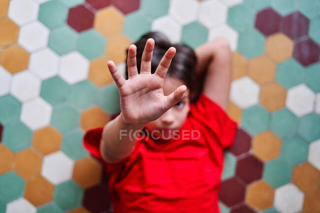 From above unhappy preteen ethnic boy lying down on floor and outstretching arm while trying to protect himself from angry parent — Stock Photo