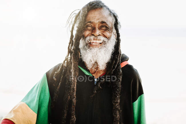 Portrait de vieux rastafari ethnique joyeux avec dreadlocks regardant la caméra dans la nature avec fond blanc — Photo de stock