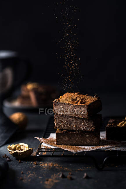 Composición de una pequeña pila de sabrosos cortes de brownie dulce con polvo sobre fondo negro - foto de stock