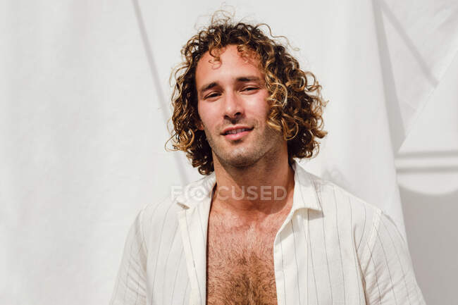 Homme torse nu souriant aux cheveux bouclés regardant la caméra sur fond blanc le jour ensoleillé — Photo de stock