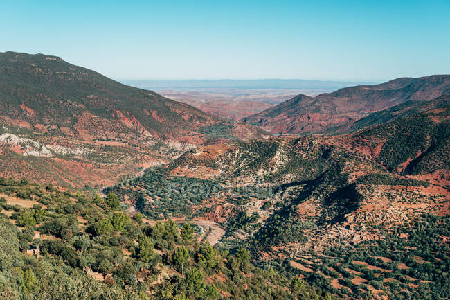 Desde arriba de colorido rojo cubierto de plantas verdes montañas y cielo azul claro en el fondo en Marruecos - foto de stock