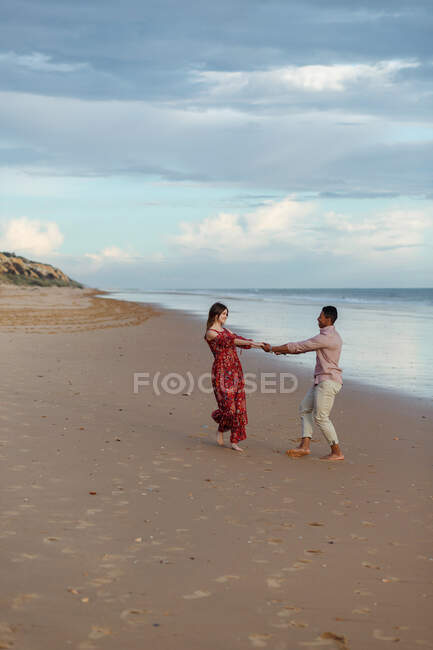Cheerful multiracial couple holding hands and walking along wet shore in summer — Stock Photo