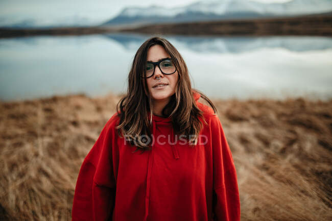 Young laughing tourist in eyeglasses with piercing and windy hair near water in sunny day on blurred background — Stock Photo
