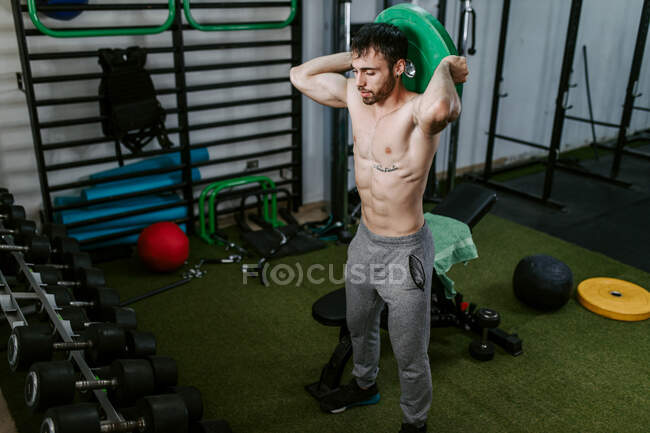 Strong male athlete exercising with heavy barbell disc during workout in gym — Stock Photo