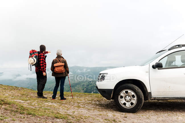 Senior woman and adult man discussing route together while standing near white vehicle during road trip in mountains — Stock Photo