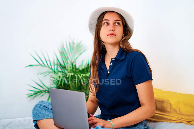 Positive young female freelancer in casual clothes sitting with legs crossed on bed and typing on laptop while working on remote project at home — Stock Photo