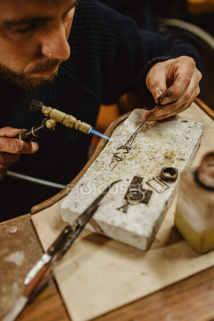 Одягнений самець золотошукач використовує тонги, роблячи маленькі металеві деталі на робочому місці в майстерні. — стокове фото