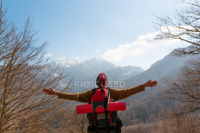 Back view of pensive female traveler with backpack standing with outstretched arms in mountains looking away — Stock Photo