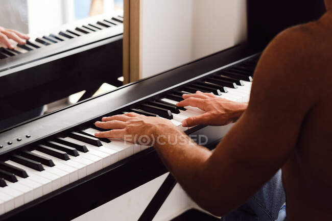 Обрізаний анонімний чоловічий музикант грає мелодію на піаніно під час репетицій вдома — стокове фото