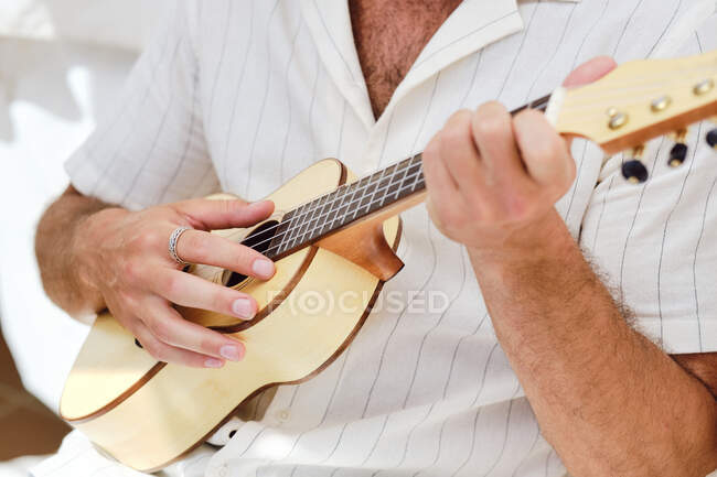 Cortado macho irreconhecível na parede branca jogando ukulele — Fotografia de Stock