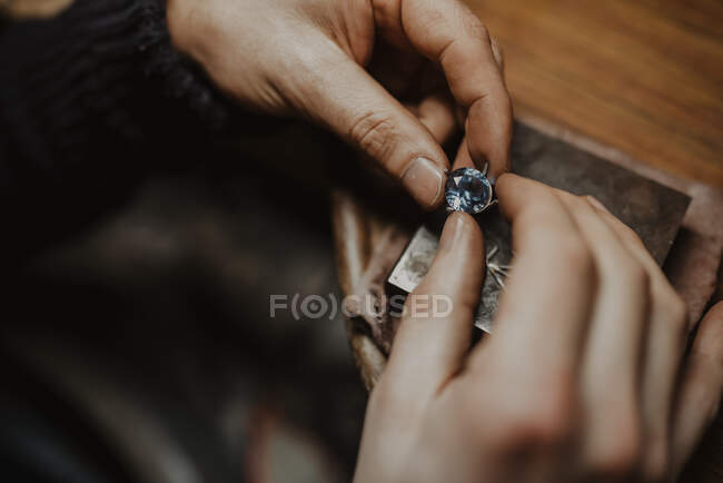 Unrecognizable goldsmith holding gem and metal ornament over table while making ring in workshop — Stock Photo