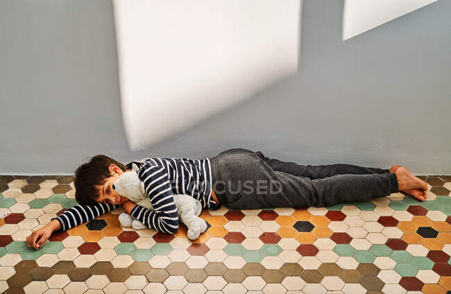 Einsamer preußischer Junge Opfer häuslicher Gewalt, der sich auf den Boden legt und Spielzeug umarmt — Stockfoto