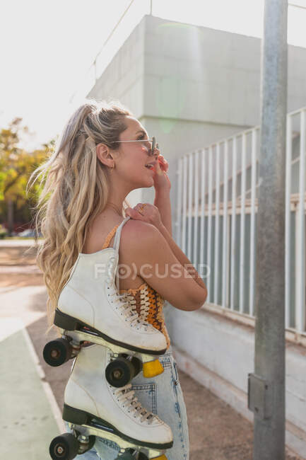 Вид сзади привлекательная молодая женщина в разорванных джинсах, несущая роликовые коньки на плече и стоящая на улице — стоковое фото