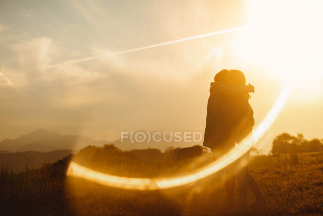 Namoradas abraçadas suavemente em pé no brilho da lente de luz do pôr do sol na natureza — Fotografia de Stock