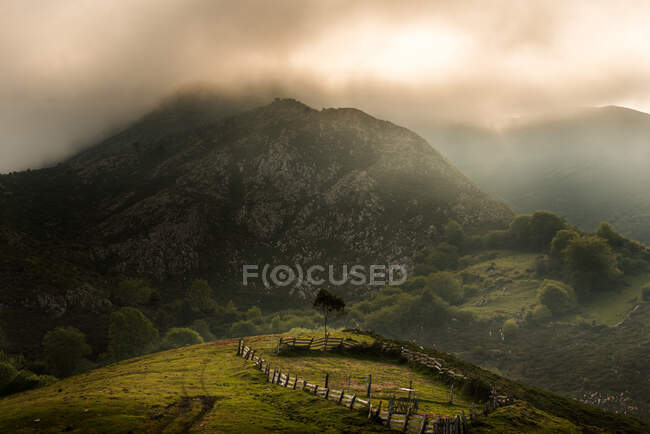 Colline erbose con recinto e montagna si trova contro cielo nuvoloso alba al mattino in campagna — Foto stock