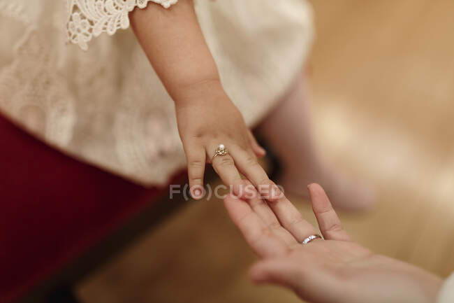 Angle élevé de la petite fille méconnaissable en robe de dentelle blanche avec bague élégante sur doigt toucher la main de la mariée anonyme — Photo de stock