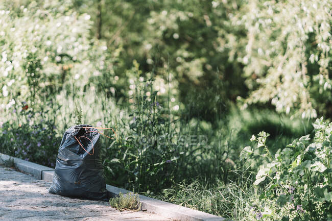 Black garbage bag placed on pathway after collecting trash in green park in summer day — Stock Photo