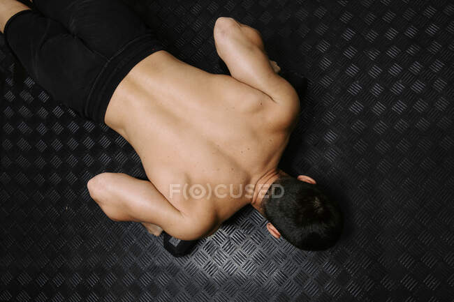 From above back view of unrecognizable male athlete with muscular naked torso doing push ups during functional workout and looking forward — Stock Photo