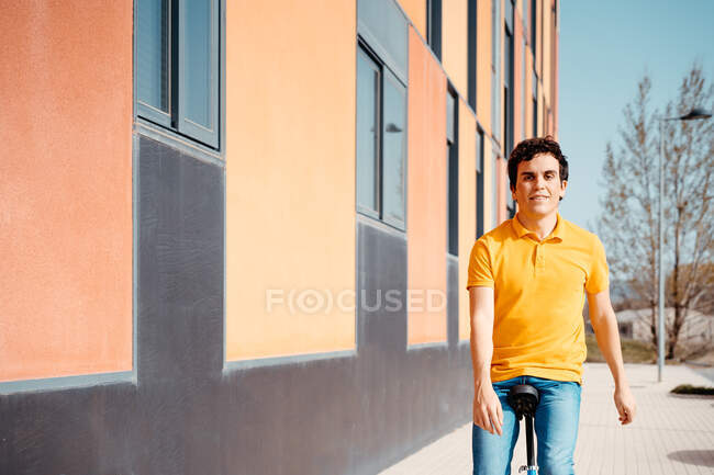 Homem feliz em desgaste casual andando de monociclo na rua urbana moderna com prédio colorido olhando para a câmera — Fotografia de Stock