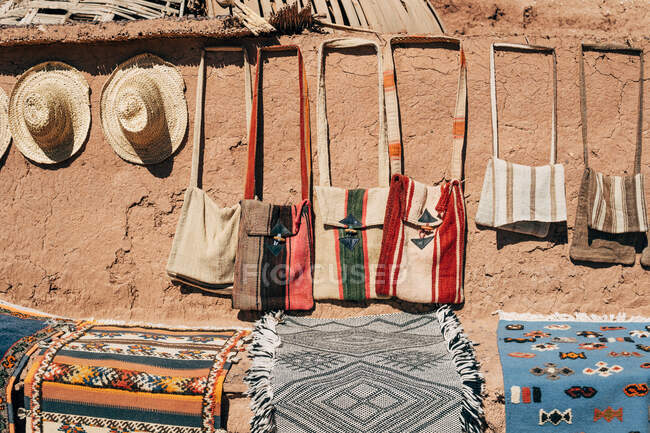 Bunte handgefertigte Mattentaschen und Strohhüte an einer steinbraunen Wand auf der Straße in Marokko — Stockfoto