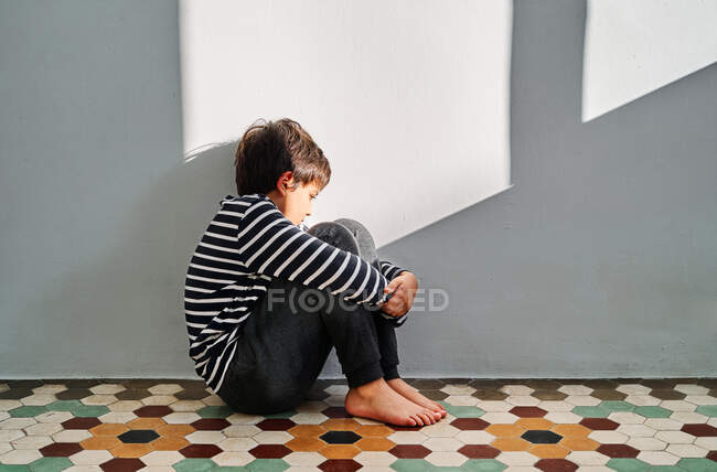 Sid view of unhappy kid sitting on floor and covering head with hands while suffering from domestic violence at home — Stock Photo