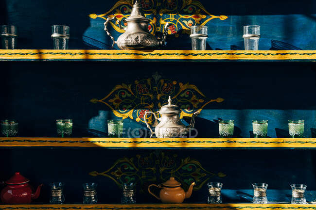 Керамические и металлические чайники со стаканами маленькие чашки на красочных полках в Марокко — стоковое фото