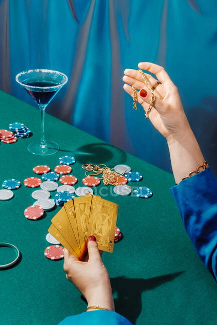 Неузнаваемая женщина урожая с драгоценностями и карточками сидит за зеленым столом и играет в покер — стоковое фото