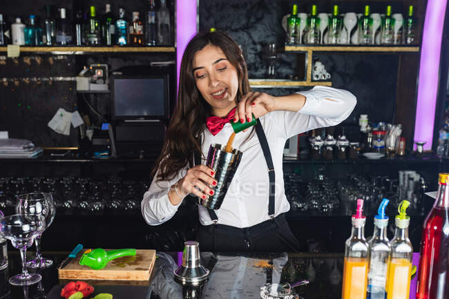 Felice barista donna in abito elegante aggiungendo zucchero nello shaker mentre prepara cocktail in piedi al bancone in un bar moderno — Foto stock