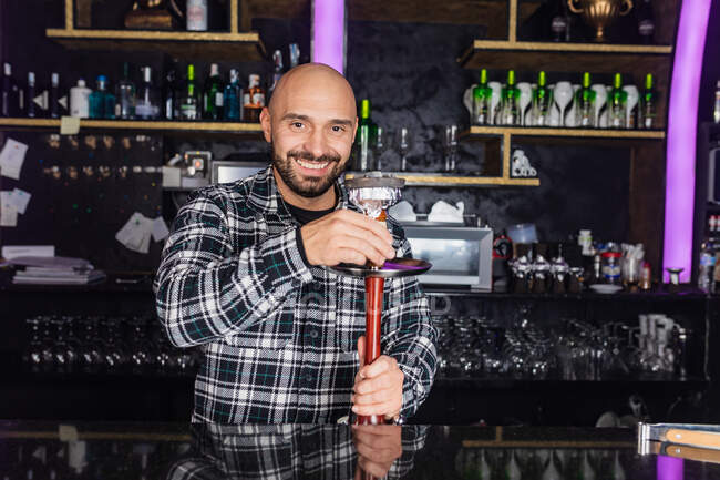 Happy male bartender preparing bowl with charcoal for hookah in a nightclub — Stock Photo